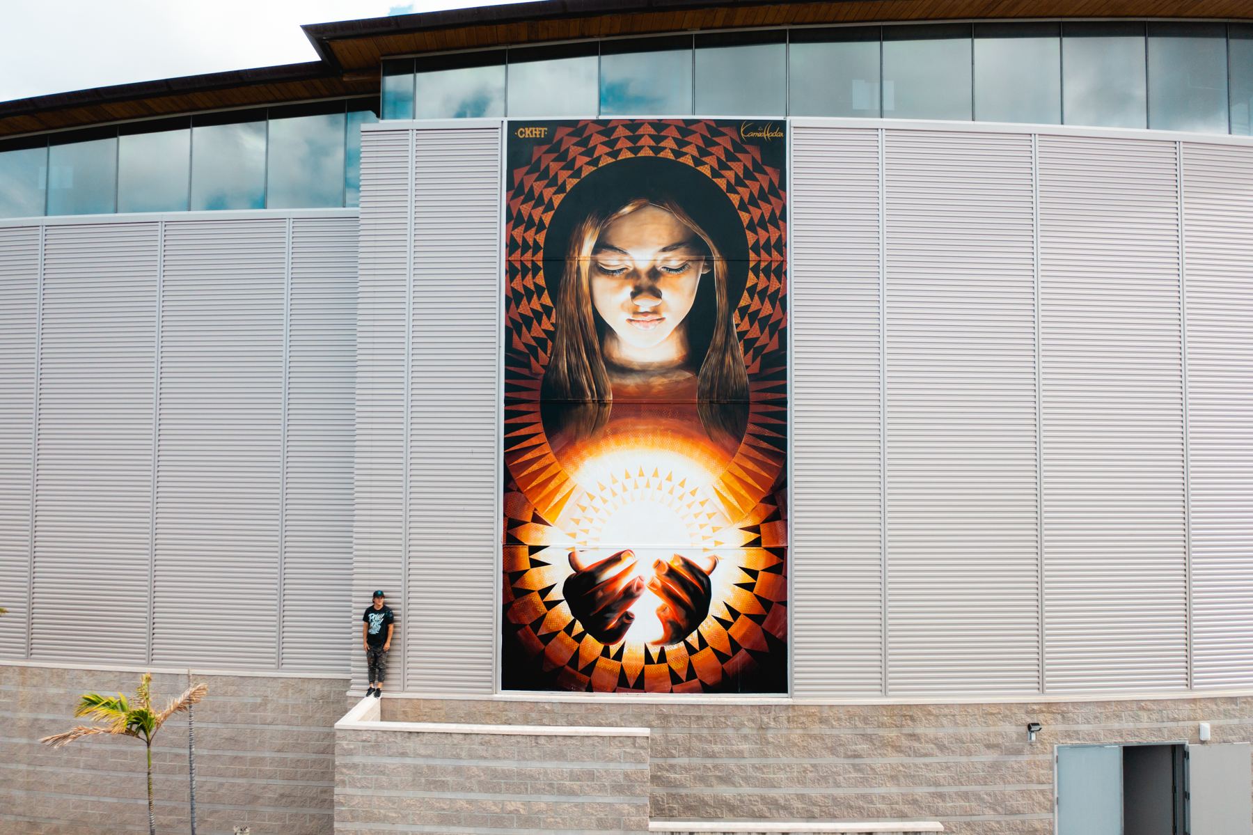 A tall mural of a girl with closed eyes holding a glowing light in her hands, painted on the Science Adventure Center.