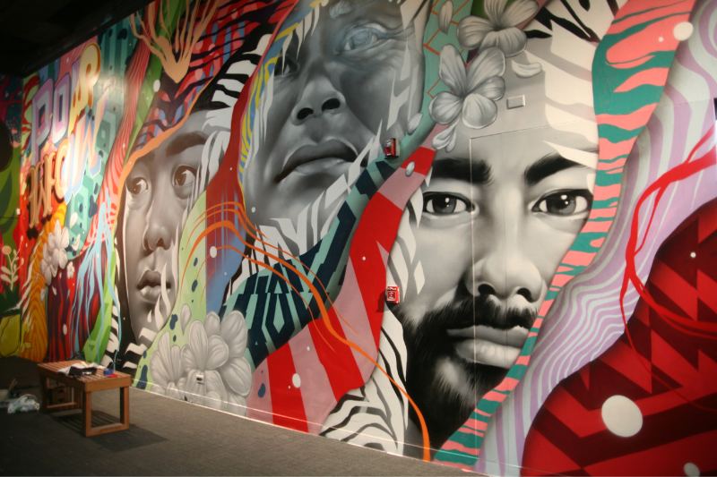 A large indoor mural of several faces rendered in grey, red and teal.