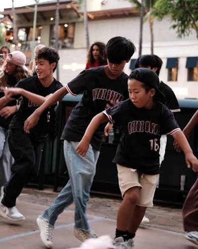 Young breakdancers in matching jerseys move together on an outdoor floor.