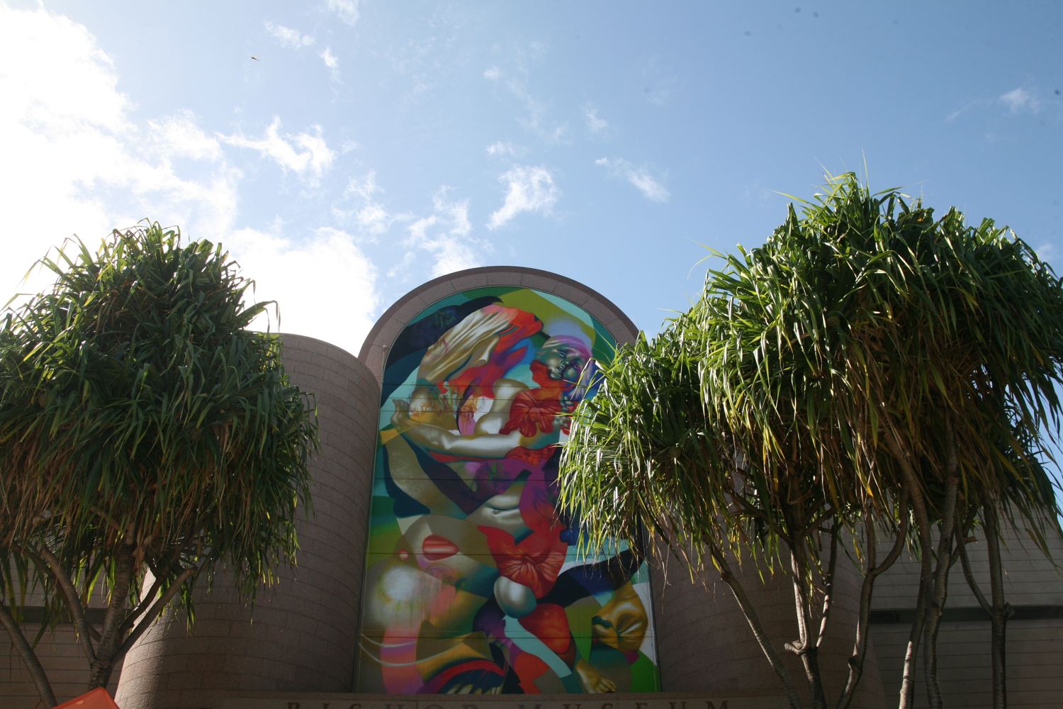The Castle Memorial Building entrance, with Hueman's towering mural of a woman's face framed by hala trees.