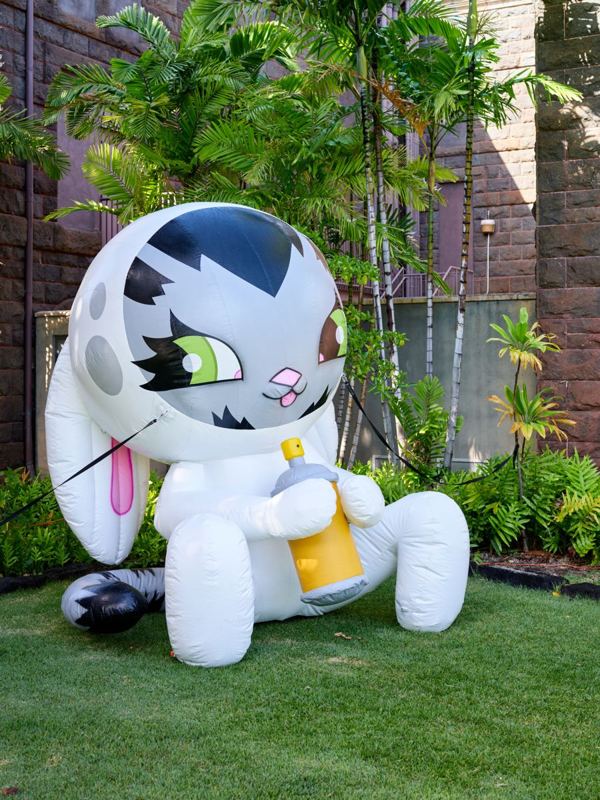 A giant inflatable cartoon cat sculpture sitting on the grass in a garden.