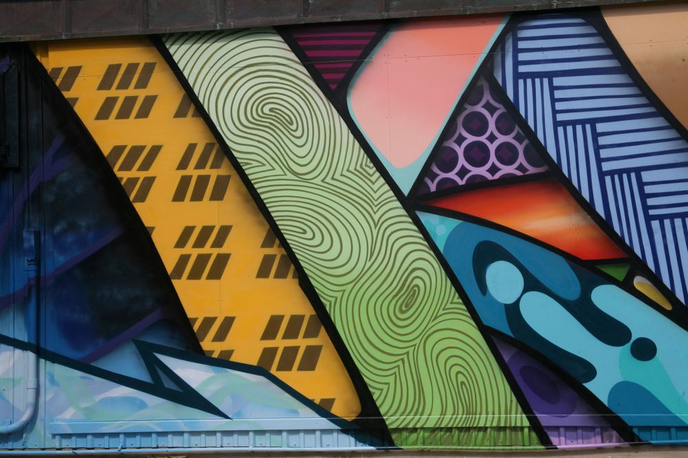 Bold abstract bands of yellow, green and blue patterns painted with spray paint.