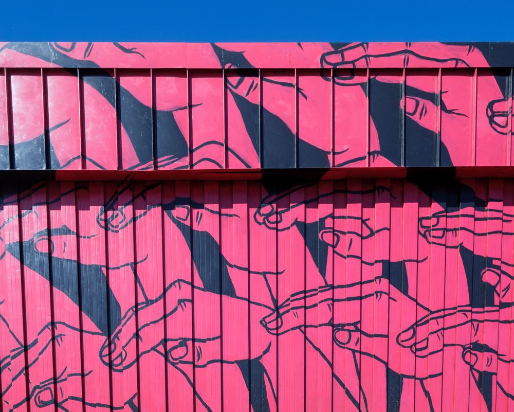 Rows of outlined hands, palms down, on a hot pink wall.