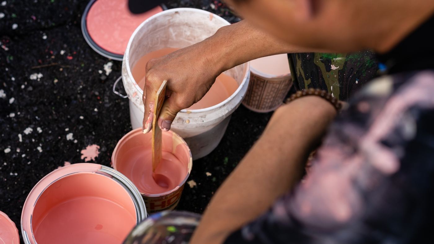 Hands stirring buckets of pink paint.