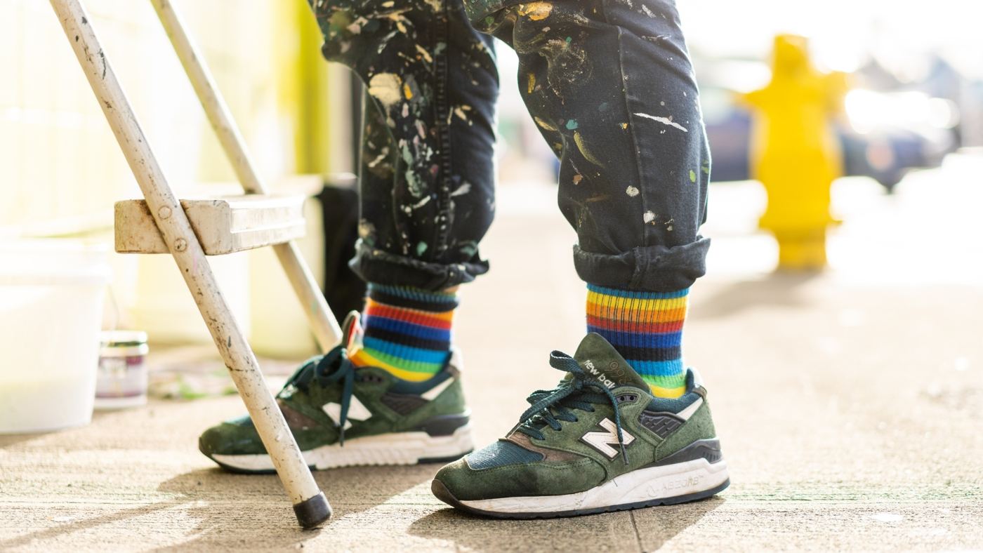 Paint-spattered pants and rainbow socks on an artist standing on a ladder.
